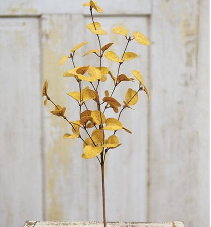 Artificial gold leaf branch on a wooden surface with a light wooden panel background