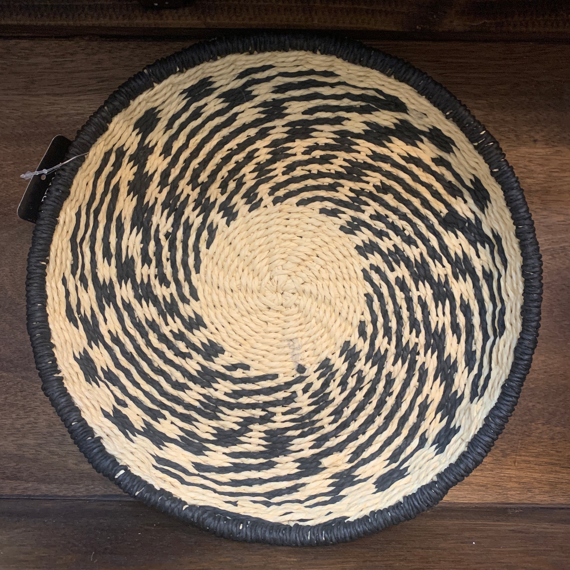 A round basket made of natural and black rope, viewed from the top, showing a patterned design.