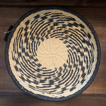 A round basket made of natural and black rope, viewed from the top, showing a patterned design.