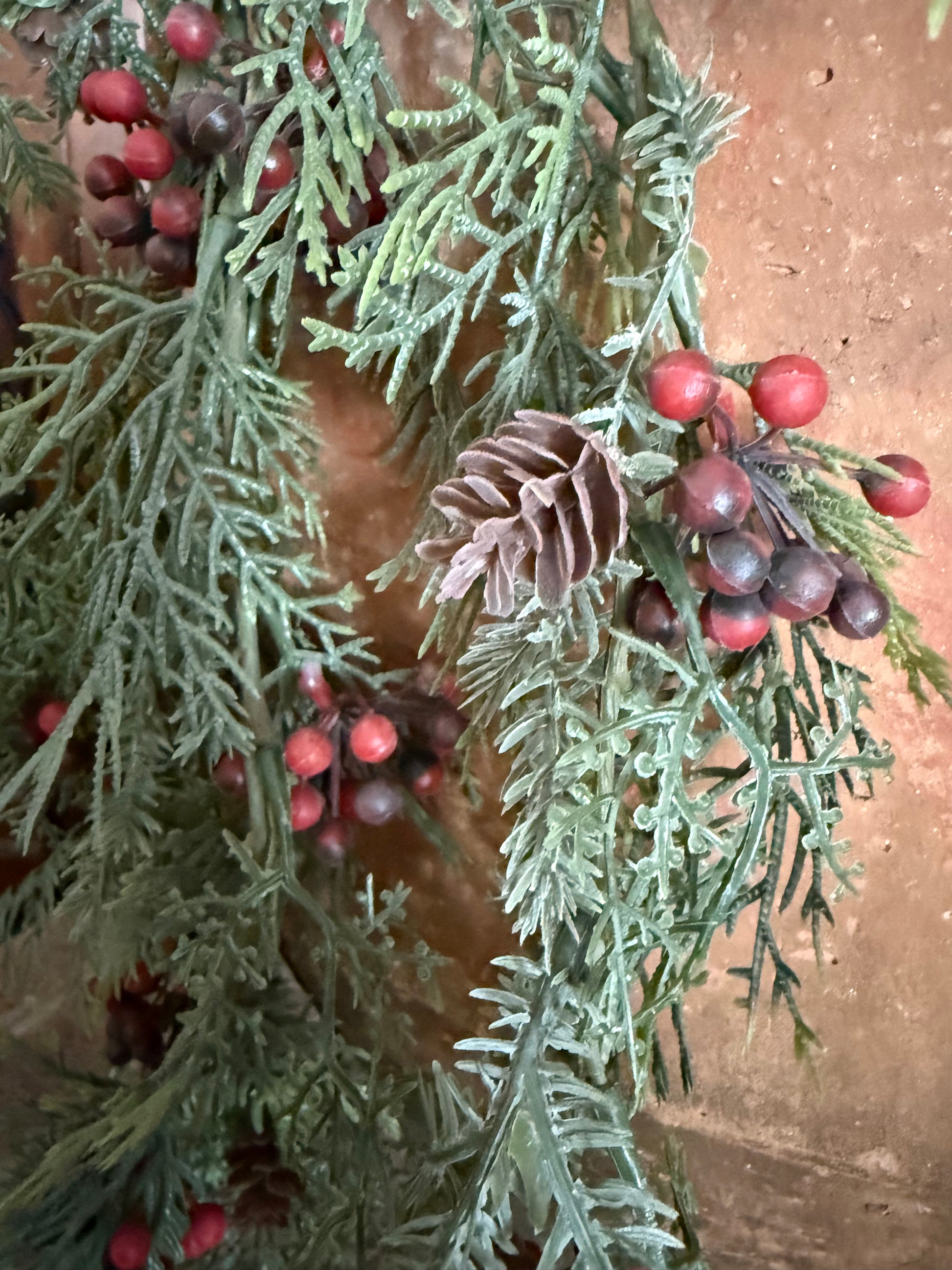 Decorative arrangement of greenery with red berries and pinecones on a textured surface.