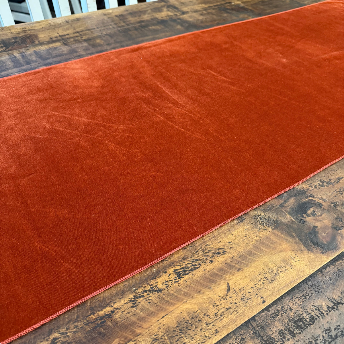 A rust-orange velvet table runner laid across a rustic wooden dining table.