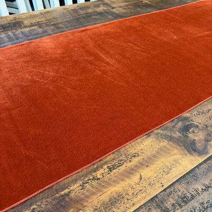 A rust-orange velvet table runner laid across a rustic wooden dining table.