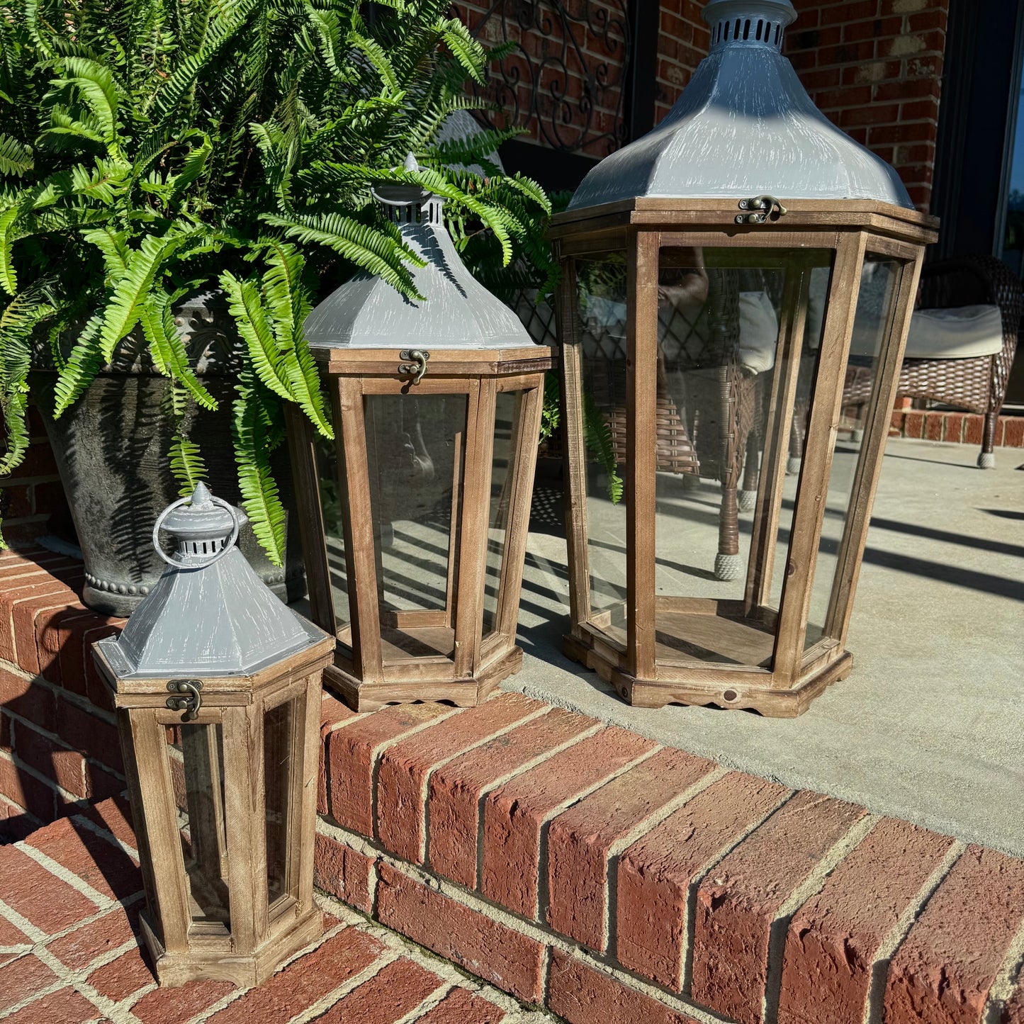 rustic wood lanterns - set of 3-Wooden lanterns on a brick ledge with plants in the background