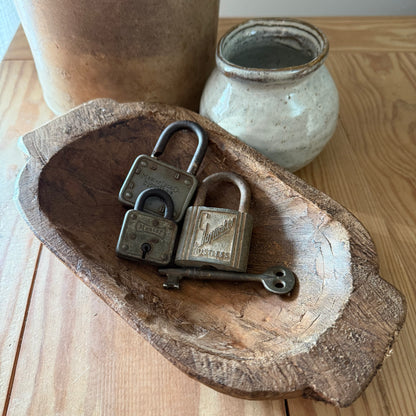 rustic wooden bowl with old locks and key sitting on wood table by ceramic vase.