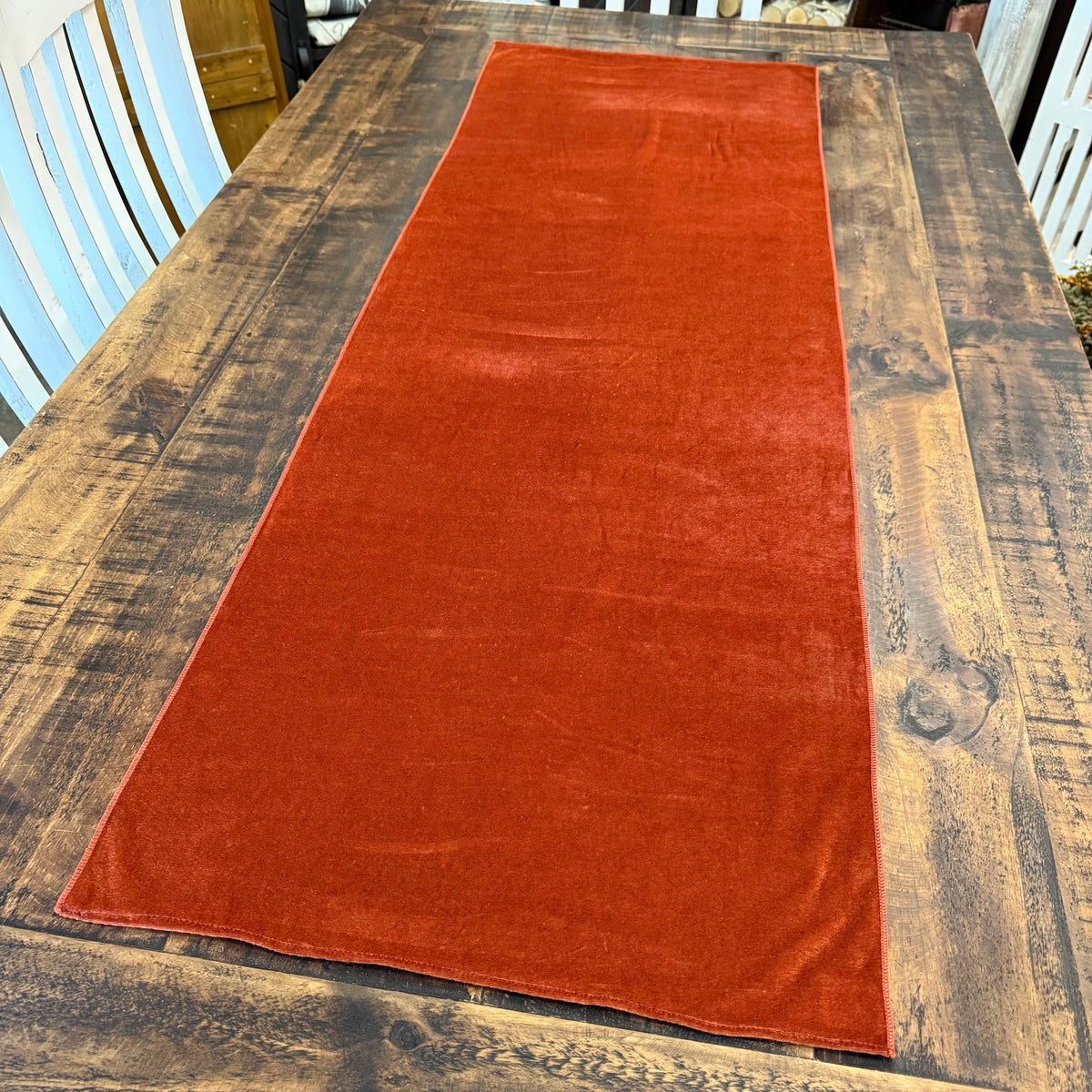 A rus fall velvet table runner laid out on a rustic dark wood dining table.