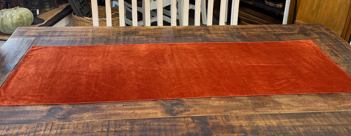 A rustic dark wood dining table with a long rust-orange velvet table runner.