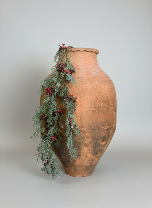 Decorative green garland with red berries draped over a textured vase.