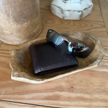 wood dough bowl with wallet and sunglasses on a wooden surface with decorative items.