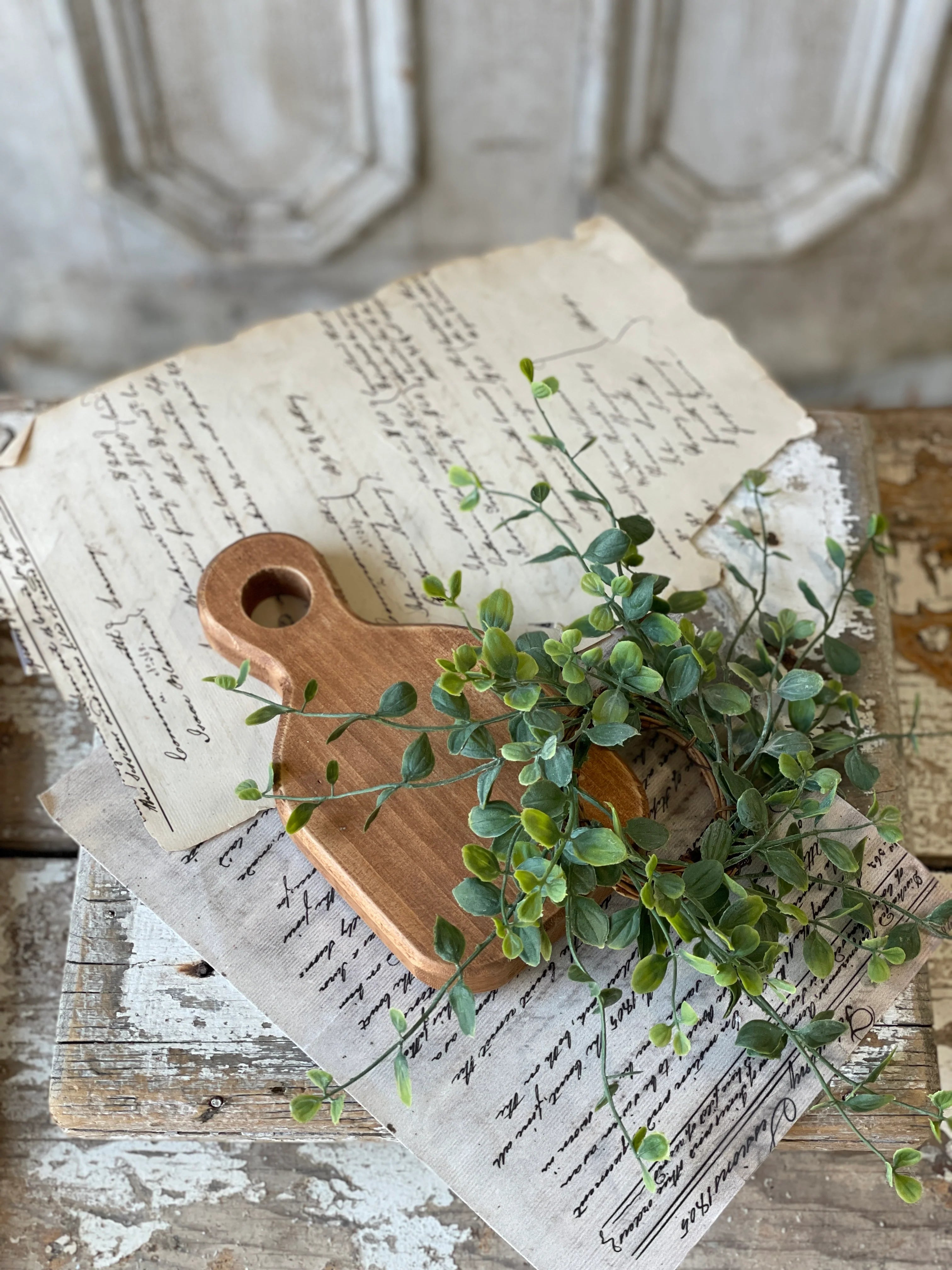 A small wooden layering plank with a handle, decorated with green artificial leaves, placed on top of a paper with writing and a map.