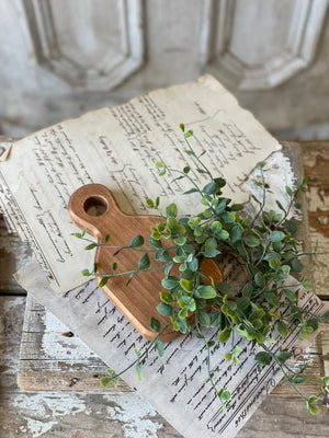 A small wooden layering plank with a handle, decorated with green artificial leaves, placed on top of a paper with writing and a map.
