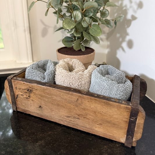 Rustic home decor -Wooden brick mold box with three textured towels and a potted plant on a dark surface. 